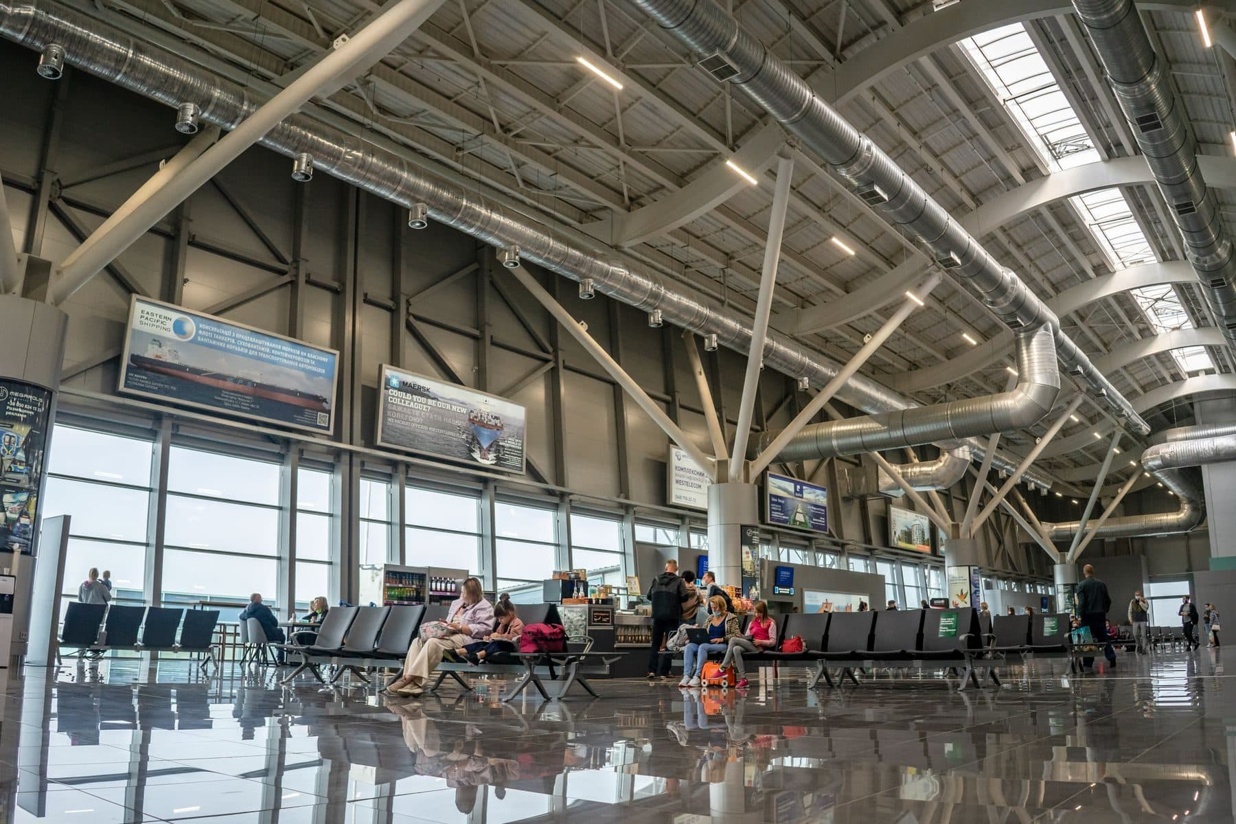 A bright airport terminal with exposed steel roof trusses and a glass wall.