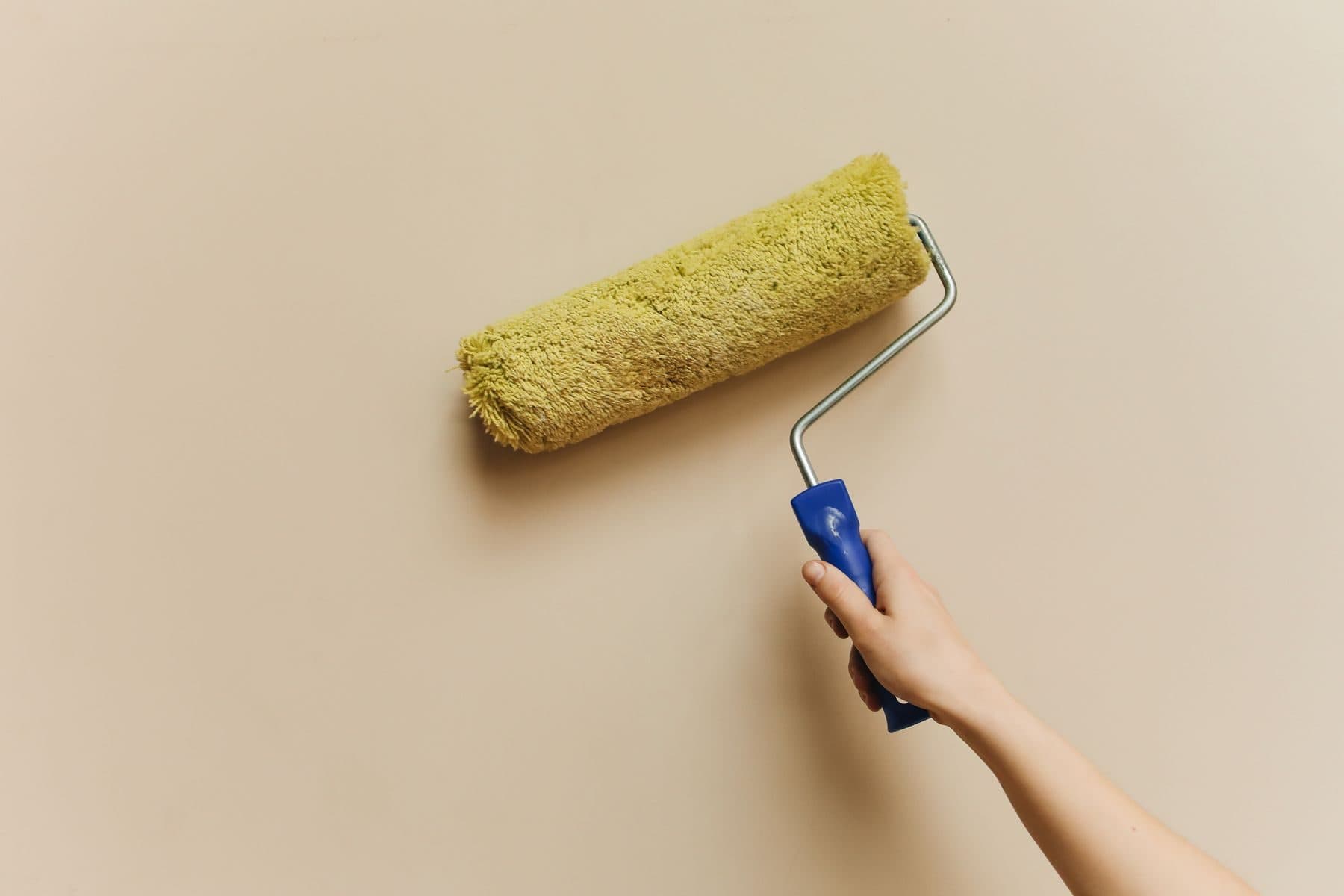 A hand rolling a yellow paint roller across a beige wall.