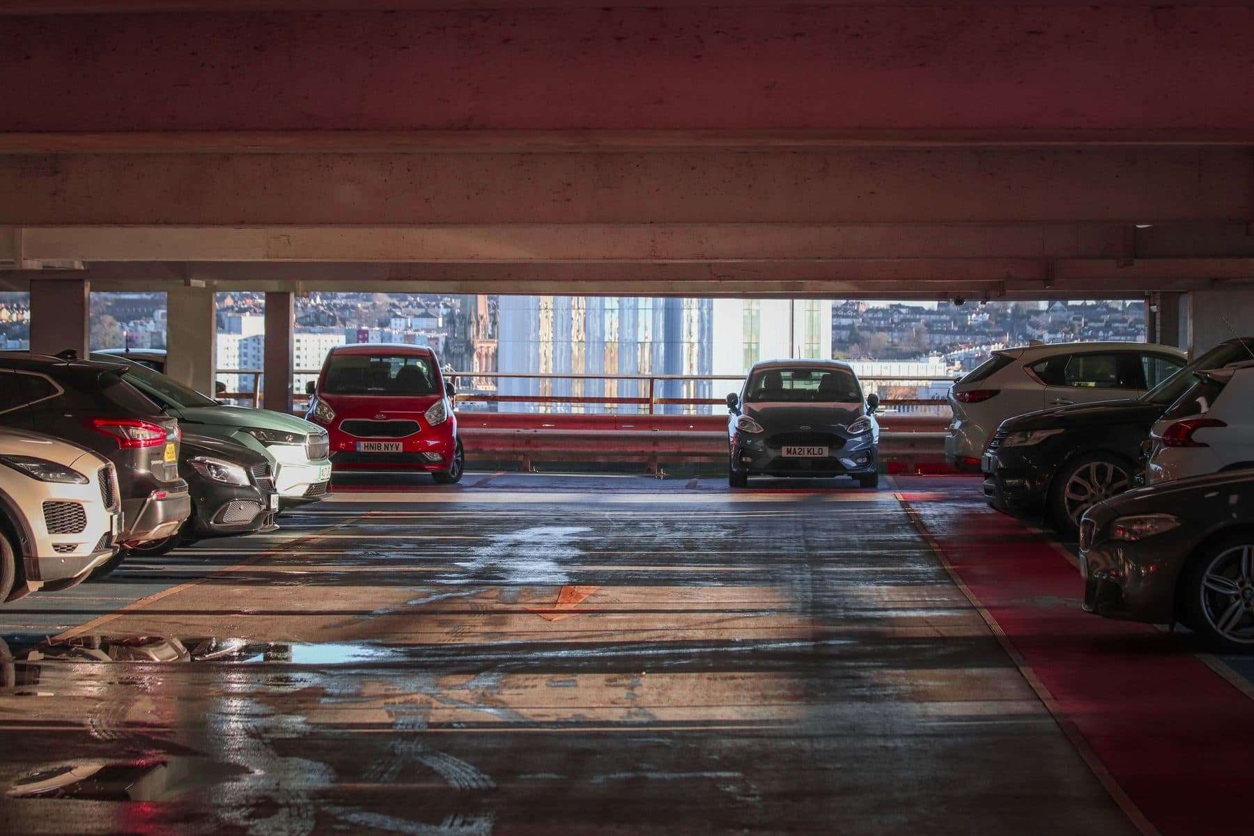 Cars parked on the upper deck of a multi-level parking garage with a city behind.