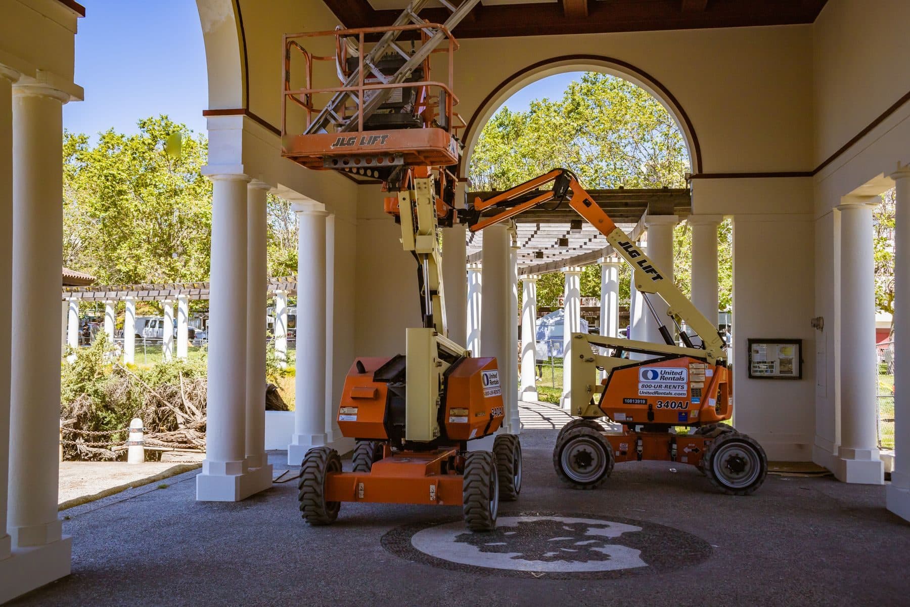 Two articulating boom lifts parked under a white arched loggia with columns.
