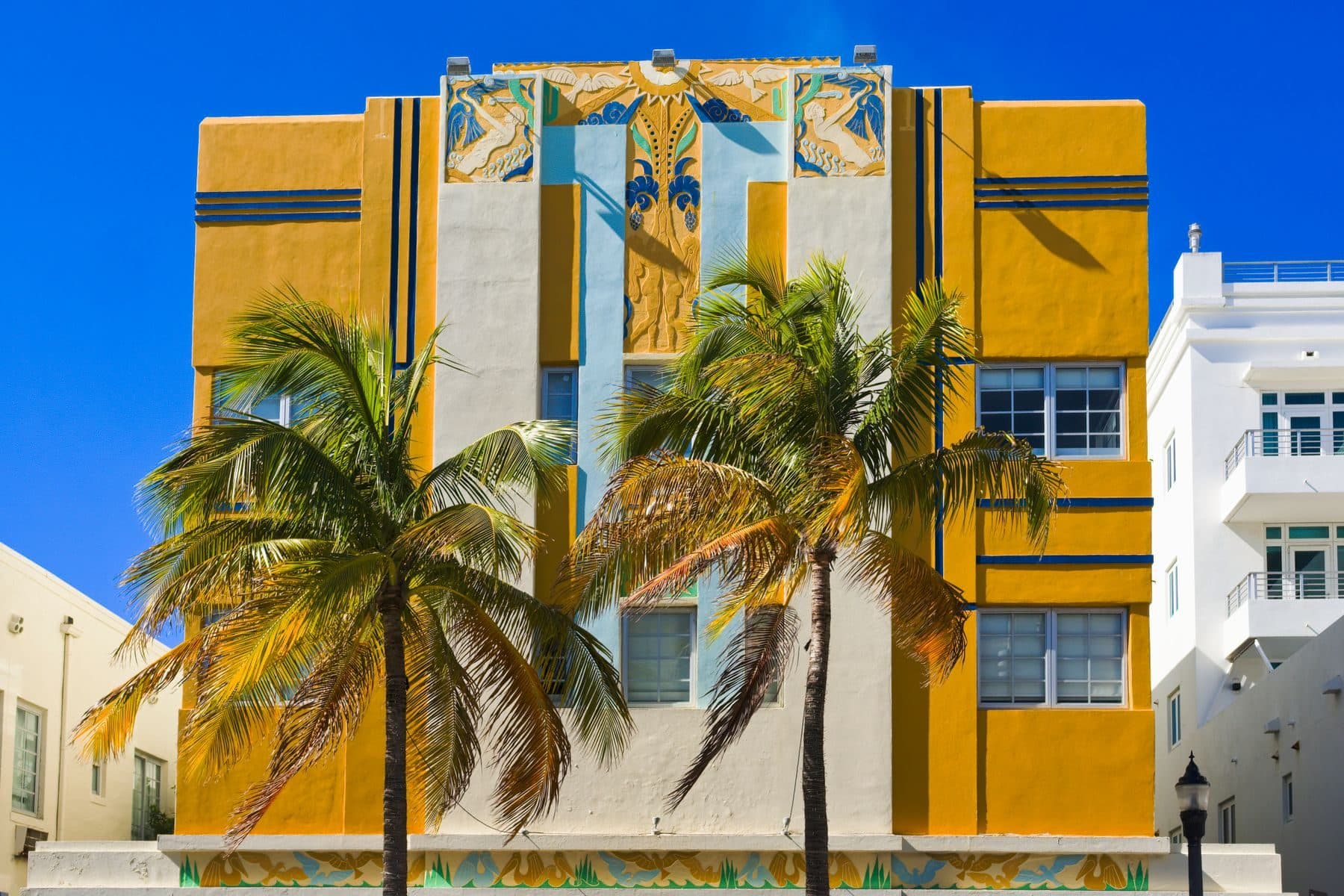 A yellow and white Art Deco building with palm trees in front.