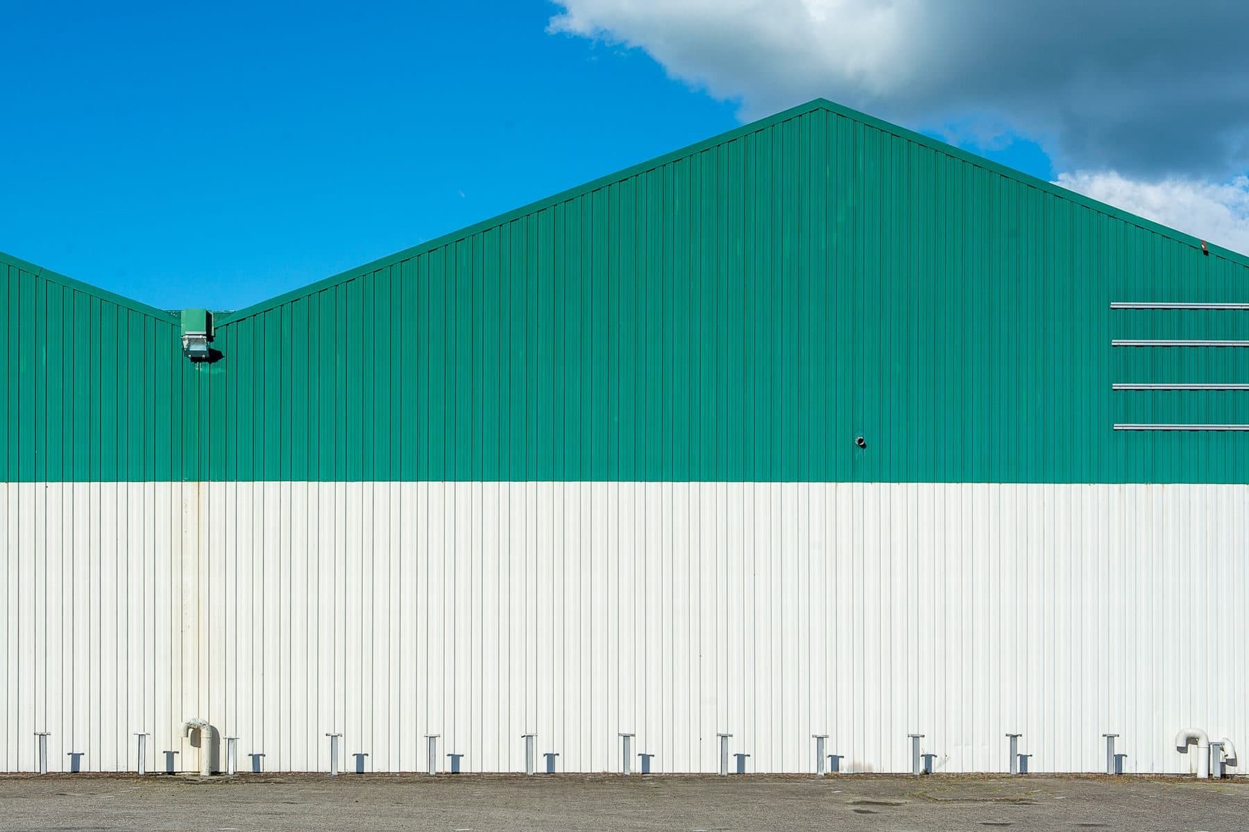 A long metal-clad warehouse painted green over white under a blue sky.